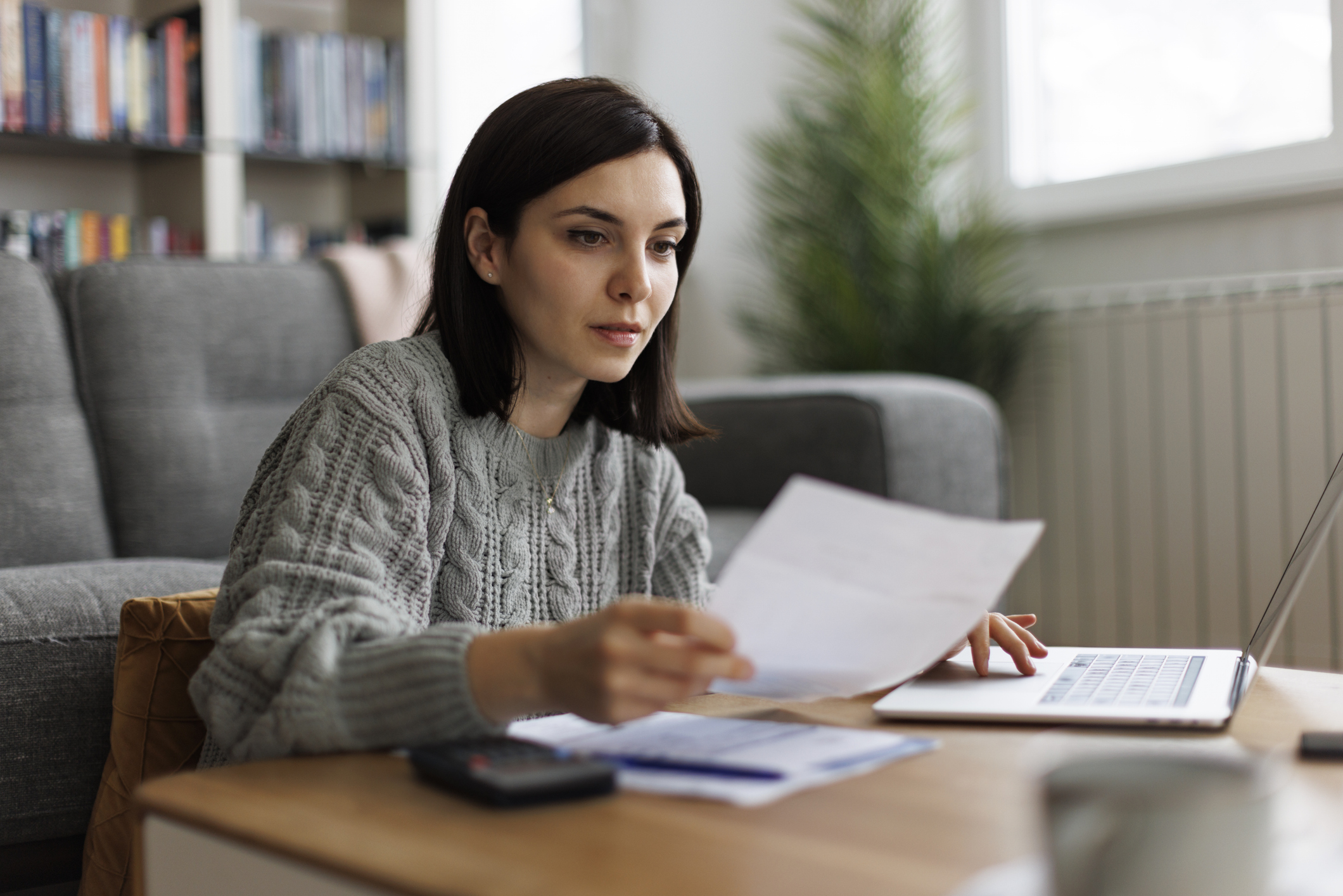 Mulher jovem confere papeis e contas. Com organização é possível driblar a ansiedade financeira